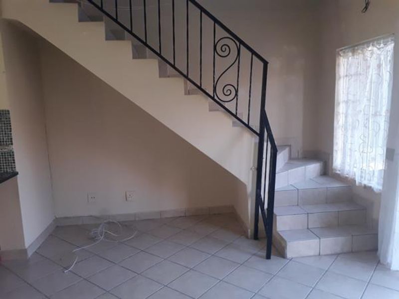 An open-plan living area featuring a staircase with a wrought iron balustrade and tiled flooring.