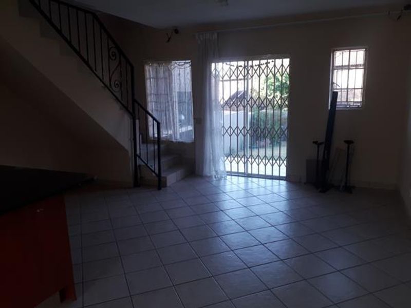 Open plan living area featuring tiled flooring, a staircase with wrought iron railing, and a sliding glass door with security gate leading outdoors.