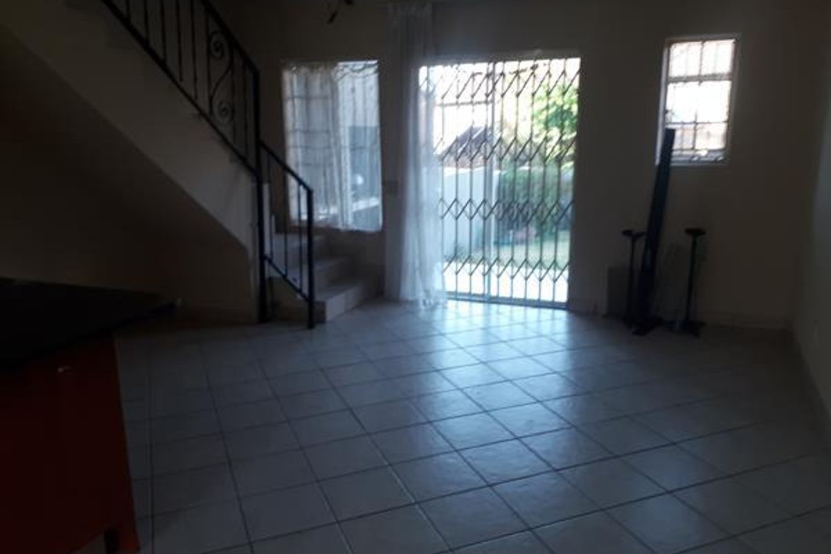 An open-plan living area featuring tiled flooring, a staircase with wrought iron railing, and a sliding glass door with security gate leading outdoors.