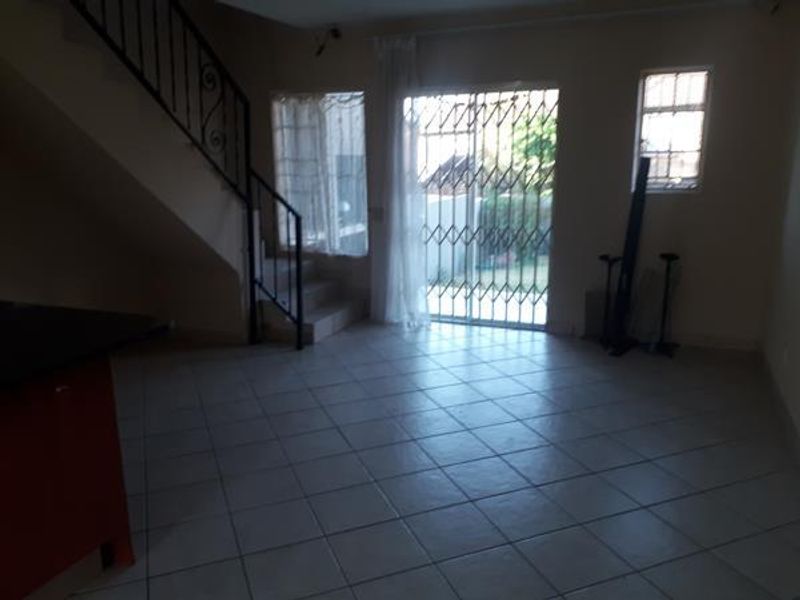 An open-plan living area featuring tiled flooring, a staircase with wrought iron railing, and a sliding glass door with security gate leading outdoors.