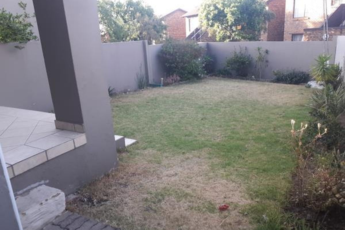 A private rear garden featuring a tiled patio area, paved walkway, and a perimeter wall, offering a blank canvas for outdoor landscaping.