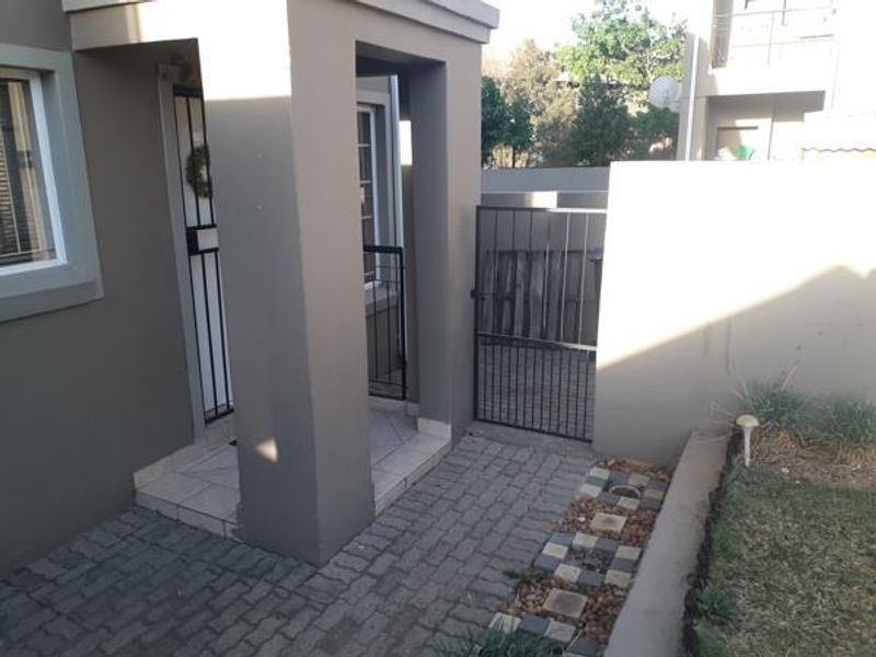 A neat front entrance area featuring a paved walkway, tiled porch, and secure metal gate access to the property.