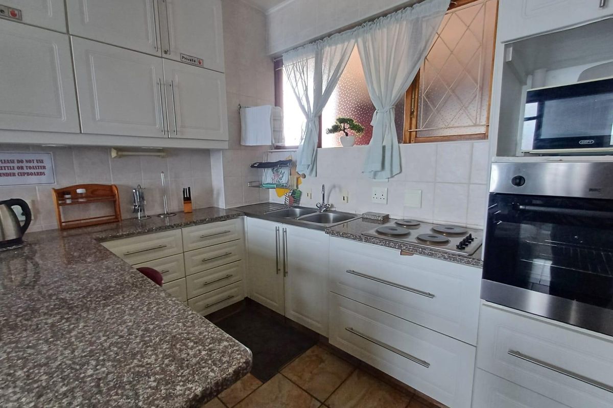 A functional kitchen featuring white cabinetry, granite countertops, a built-in oven, electric hob, and tiled finishes throughout.