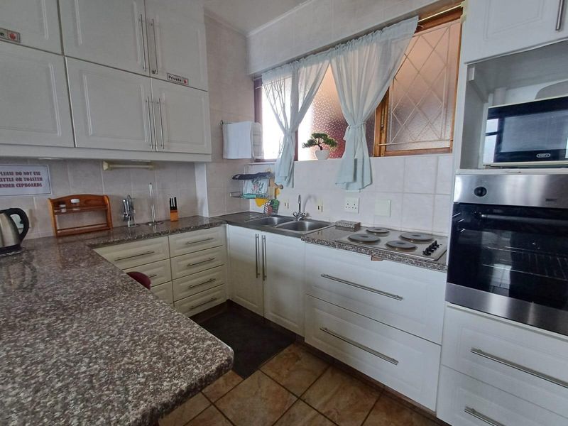A functional kitchen featuring white cabinetry, granite countertops, a built-in oven, electric hob, and tiled finishes throughout.