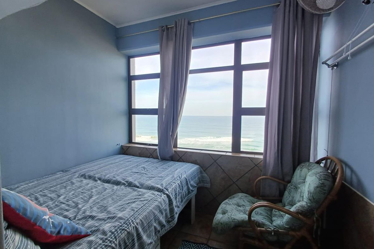 A bedroom featuring large windows with direct ocean views, tiled flooring, and a tiled window sill, offering a bright and coastal living space.