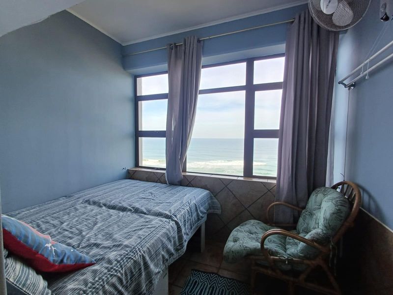 A bedroom featuring large windows with direct ocean views, tiled flooring, and a tiled window sill, offering a bright and coastal living space.