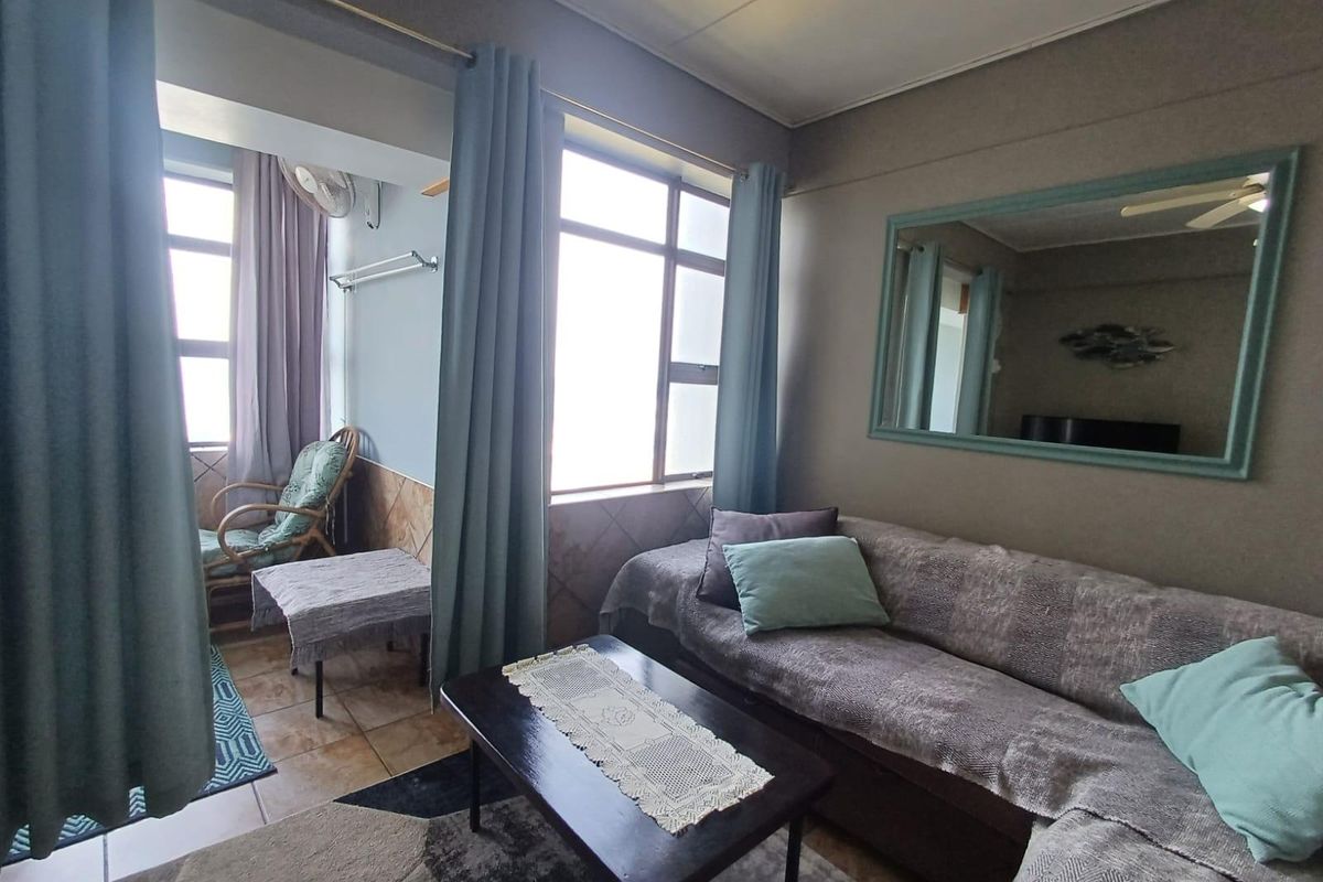 A living room area featuring tiled flooring, large windows providing natural light, and a built-in wall mirror, connected to an adjacent sunroom space.