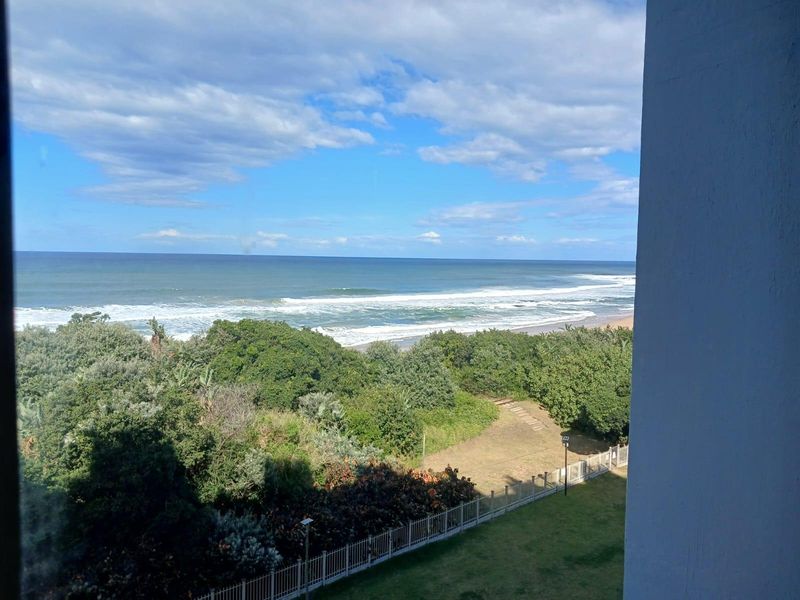 A scenic elevated view overlooking the coastal landscape, lush greenery, and the ocean, framed by the building structure.