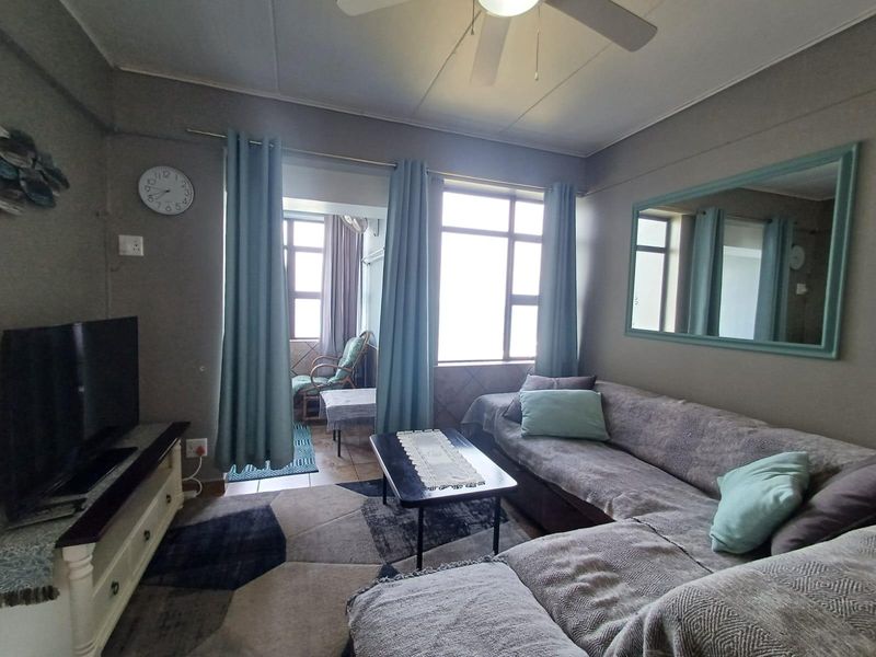 A comfortable living room featuring a ceiling fan, large windows allowing natural light, and direct access to an adjoining balcony area.