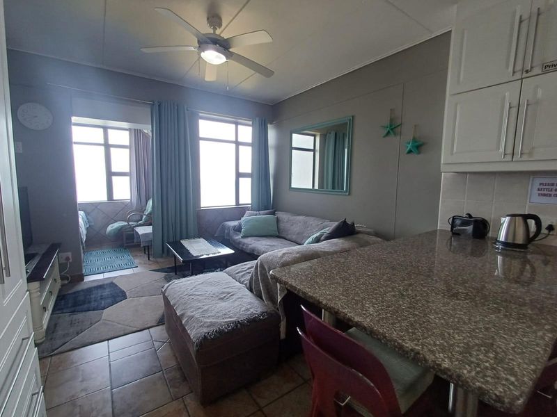Open-plan living area featuring a kitchen with granite countertops, tiled flooring, and a ceiling fan, seamlessly connecting to a bright lounge and balcony space.