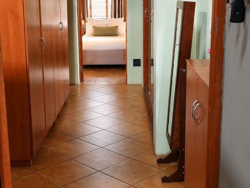 A hallway featuring tiled flooring, built-in wooden cupboards, and an exposed thatch roof, leading into a bedroom.