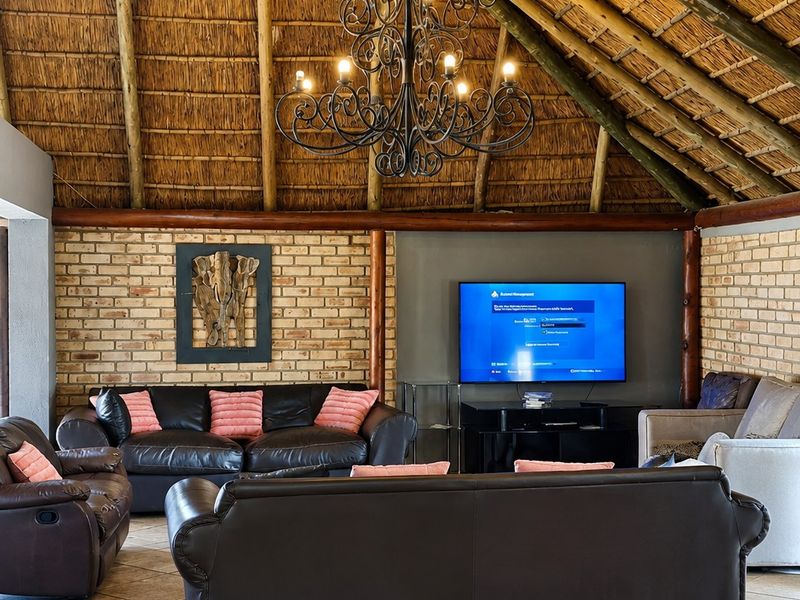 Spacious living room featuring a high vaulted thatched ceiling with exposed timber rafters, exposed brick walls, and ceramic tiled flooring.