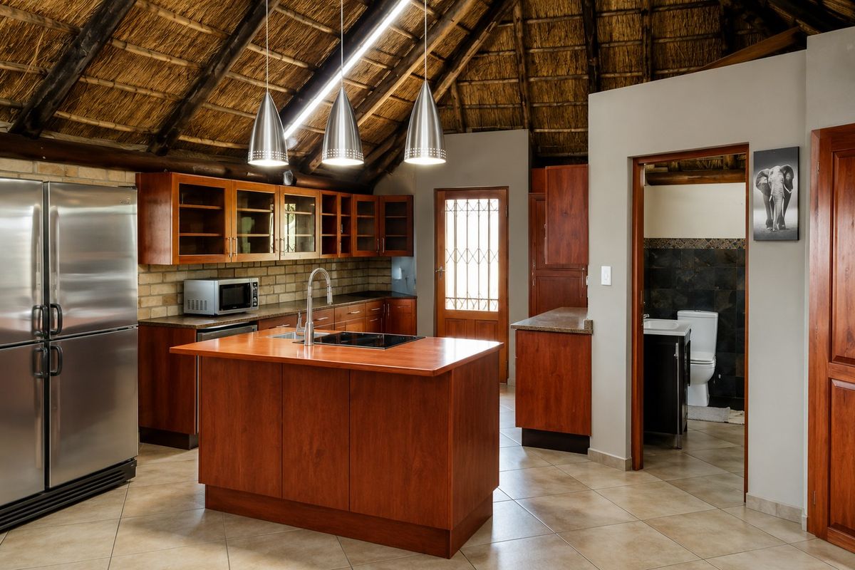Spacious kitchen featuring a unique thatched roof, wooden cabinetry, a central island with a hob, and direct access to an adjoining bathroom.