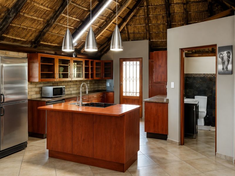 Spacious kitchen featuring a unique thatched roof, wooden cabinetry, a central island with a hob, and direct access to an adjoining bathroom.