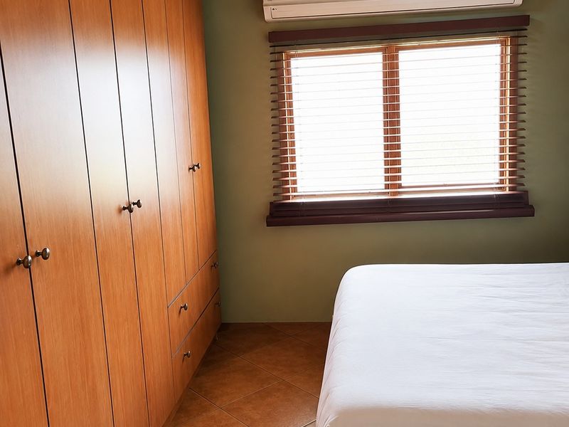 A well-maintained bedroom featuring built-in wooden cupboards, a split-system air conditioner, and a unique thatched ceiling with exposed timber beams.