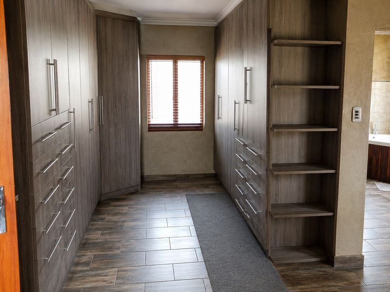 A spacious walk-in dressing room featuring extensive built-in cabinetry with modern wood-grain finishes, tiled flooring, and a window with venetian blinds.