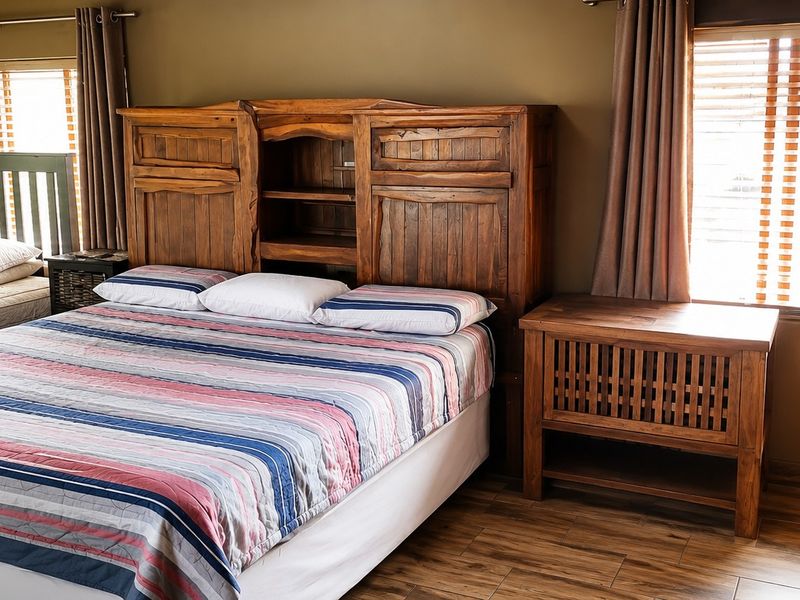 A bedroom featuring wooden flooring, window blinds, and curtain rails, providing a functional space with natural light.