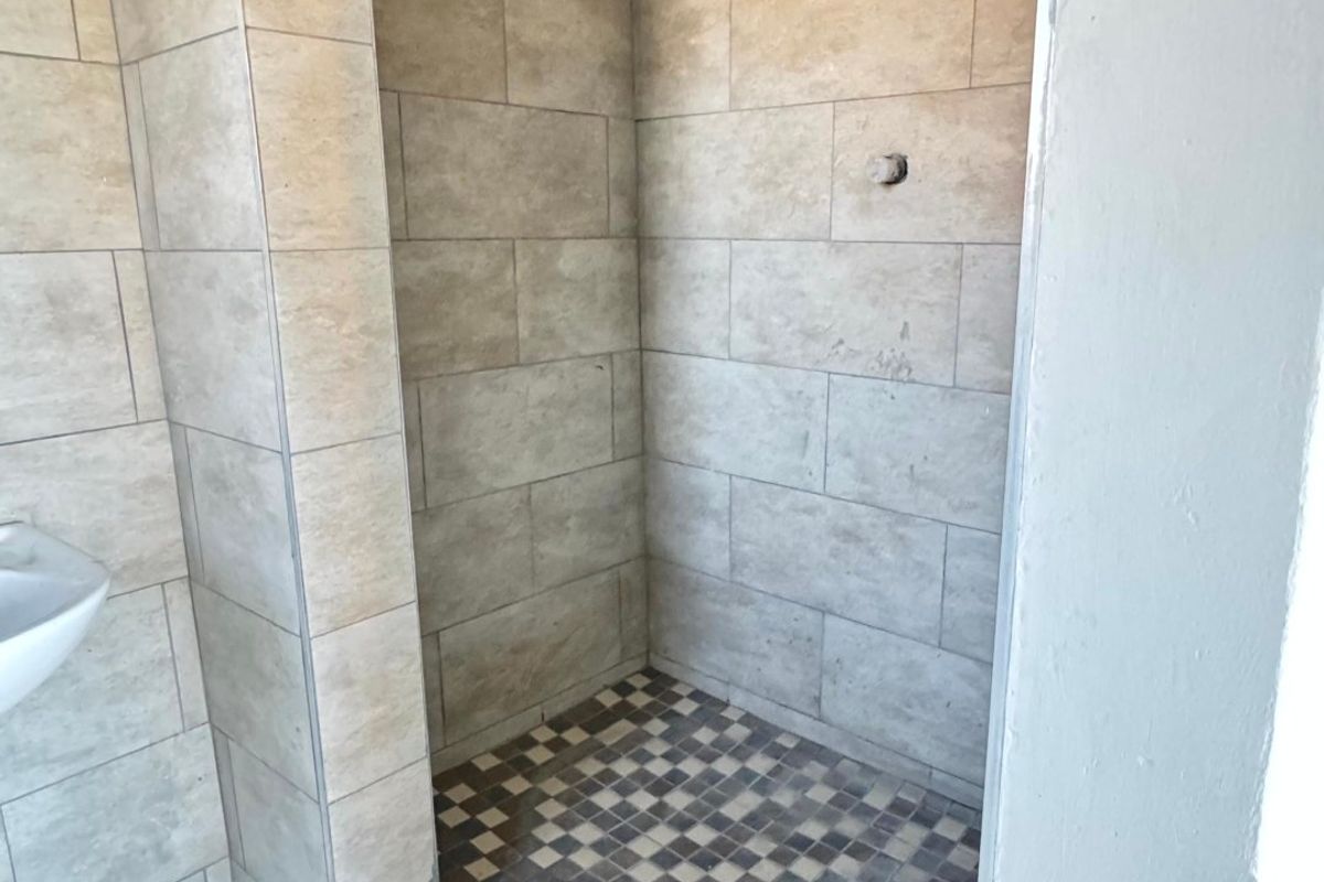 A walk-in shower area featuring neutral wall tiles, mosaic floor tiling, and a pedestal basin, currently requiring a new shower mixer installation.