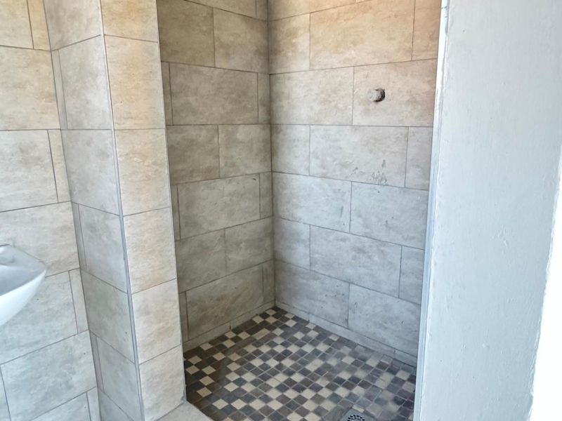A walk-in shower area featuring neutral wall tiles, mosaic floor tiling, and a pedestal basin, currently requiring a new shower mixer installation.