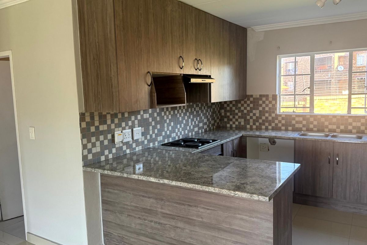 A functional kitchen featuring wood-look laminate cabinetry, granite countertops, a gas hob with extractor, and a tiled backsplash, ready for final finishing touches.