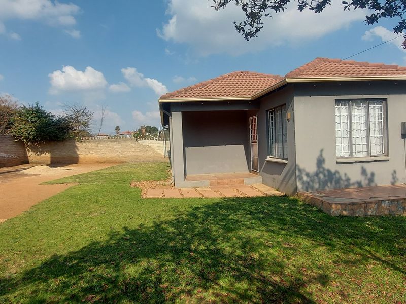 Rear view of a detached house featuring a covered patio, tiled roof, and a spacious garden area enclosed by brick boundary walls.