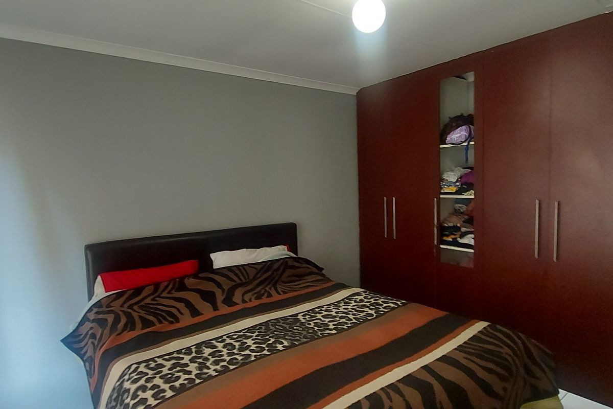 A bedroom featuring a large dark wood built-in wardrobe with integrated shelving and neutral grey wall finishes.