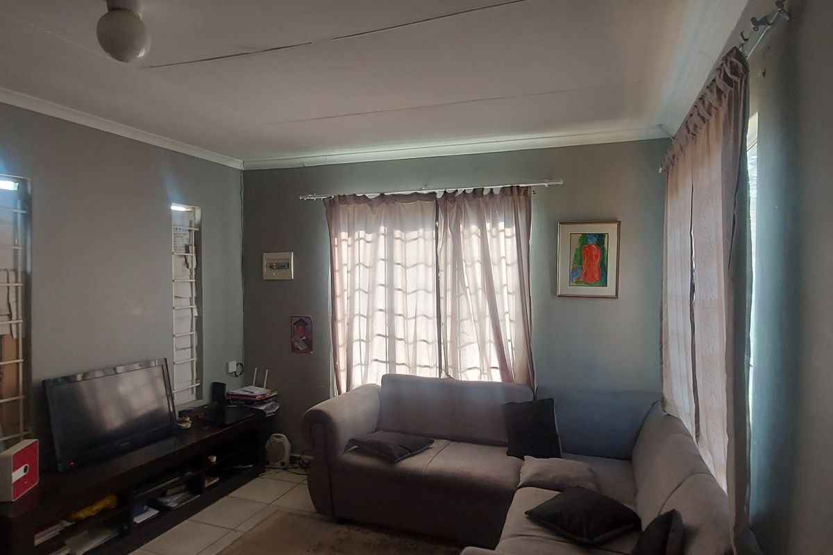 A living room featuring tiled flooring, security bars on windows, and a coved ceiling, currently showing signs of wear including ceiling cracks.