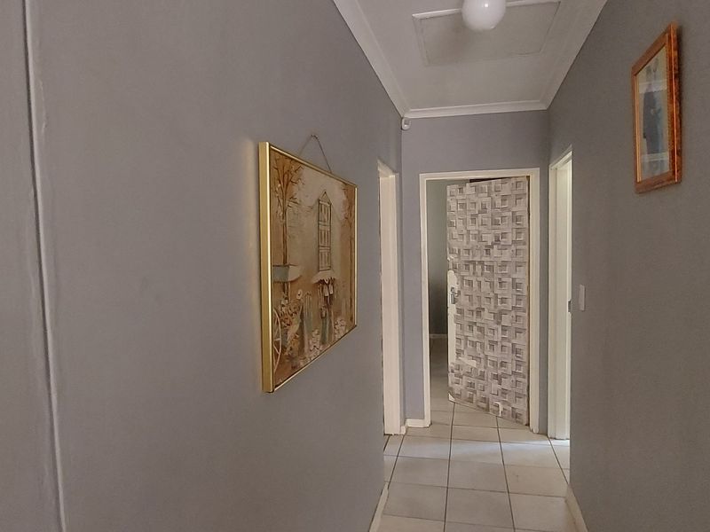 A neutral-toned hallway featuring tiled flooring and a ceiling access hatch, providing access to multiple rooms within the home.