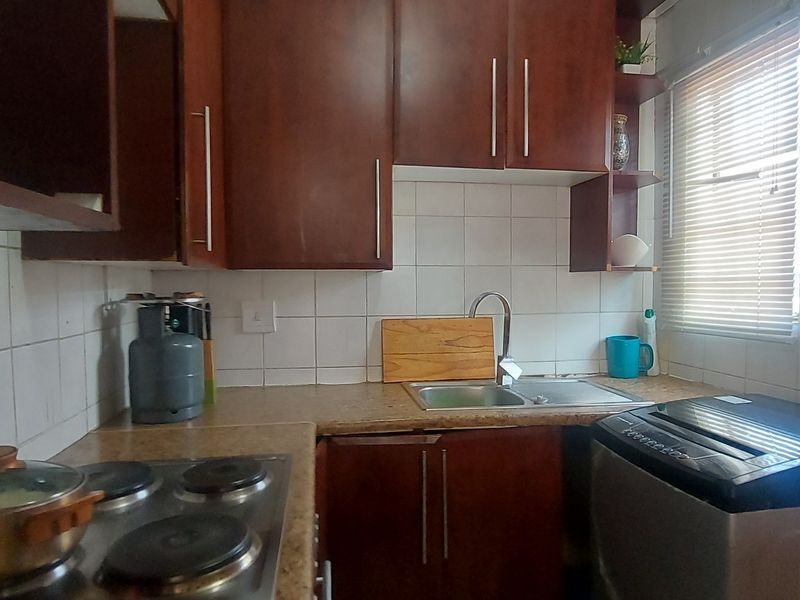 Compact kitchen featuring dark wood-finish cabinetry, tiled backsplash, stainless steel sink, and integrated electric hob with ample counter space.