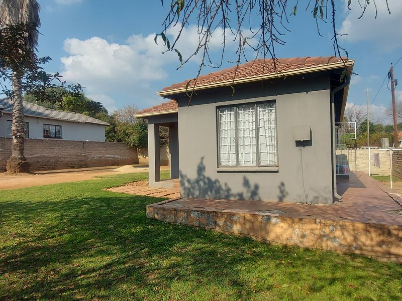 Rear view of the house featuring a paved patio area, a lawn, and brick boundary walls.