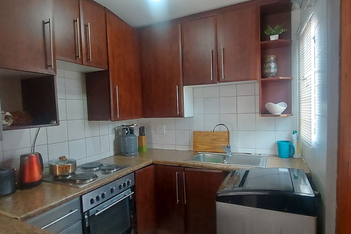 Compact kitchen featuring dark wood-look cabinetry, laminate countertops, built-in oven, electric hob, and tiled splashback.