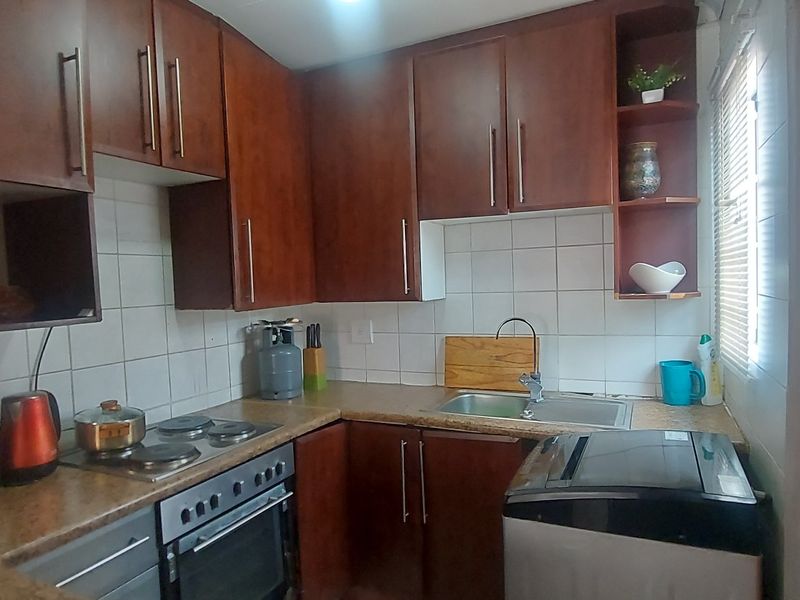 Compact kitchen featuring dark wood-look cabinetry, laminate countertops, built-in oven, electric hob, and tiled splashback.