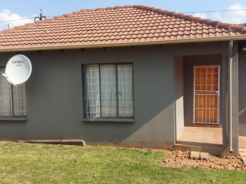Front elevation of a single-story house featuring a tiled roof, security gates, and window burglar bars, set on a residential plot.