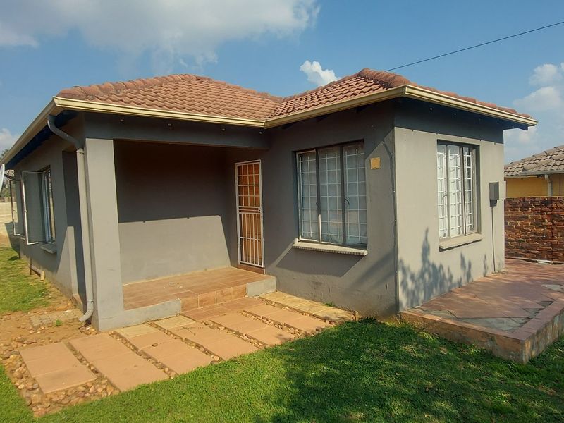 Rear view of a single-story house featuring a tiled roof, covered patio area, and a brick boundary wall in a garden setting.
