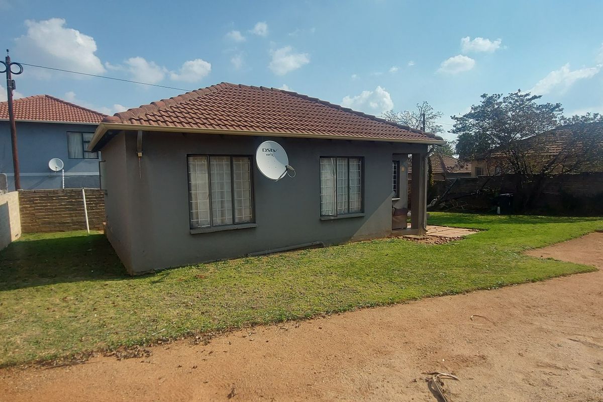 Rear view of a detached house featuring a tiled roof, security bars on windows, and a small paved patio area set within a garden.