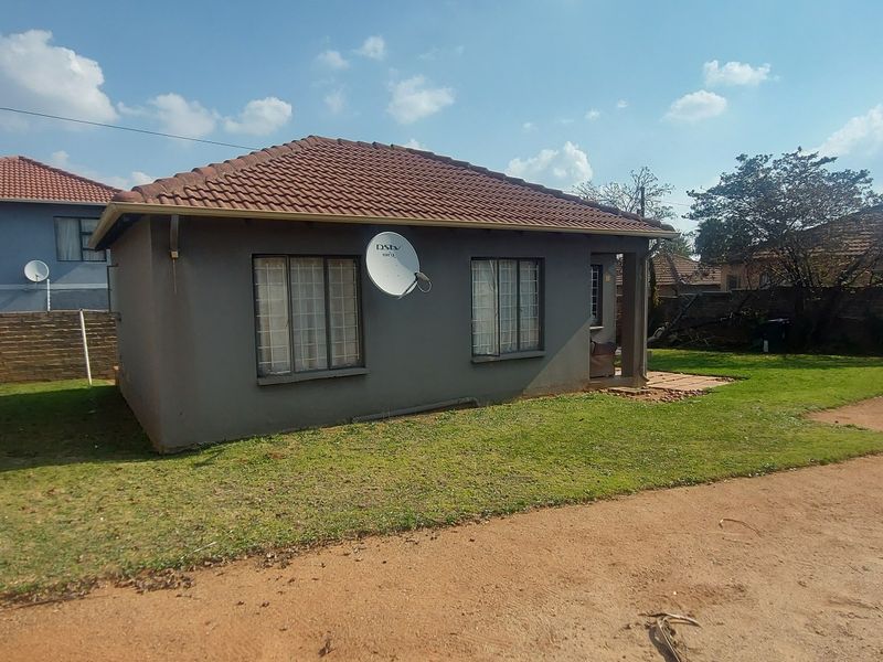Rear view of a detached house featuring a tiled roof, security bars on windows, and a small paved patio area set within a garden.