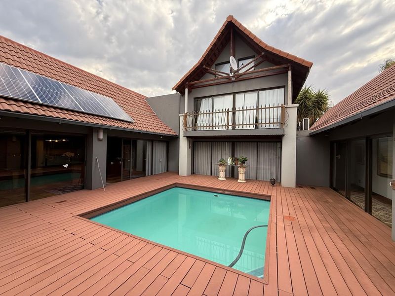 A well-maintained outdoor pool area featuring timber decking, a swimming pool, and a multi-level home exterior with solar panels and a balcony.