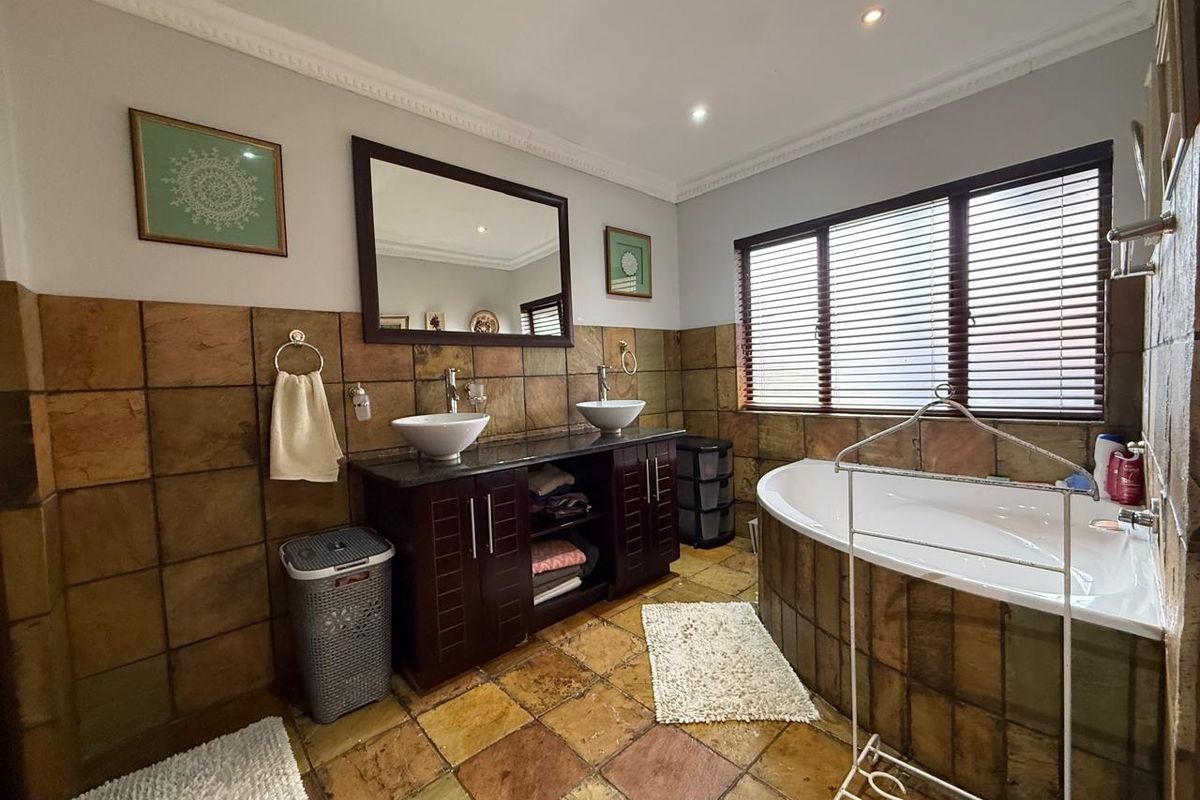 A spacious bathroom featuring a double vanity with vessel sinks, a built-in bathtub, and rustic stone wall and floor tiling.