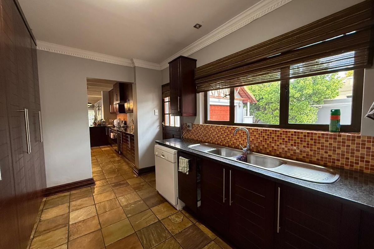 Functional kitchen featuring dark wood cabinetry, granite countertops, a double stainless steel sink, and a mosaic tile backsplash with stone flooring.