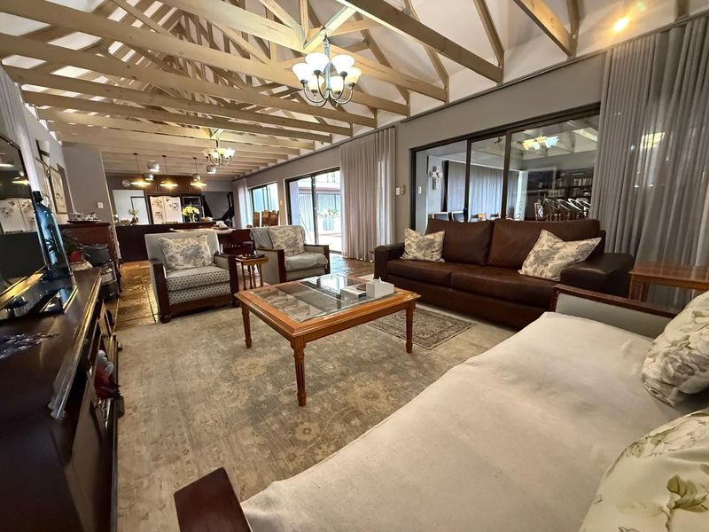 Spacious open-plan living area featuring high vaulted ceilings with exposed timber trusses, tiled flooring, and large sliding glass doors leading to the outdoors.