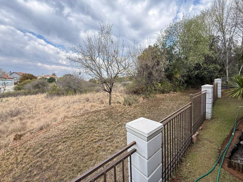A view of the rear garden area featuring metal perimeter fencing with concrete pillars, overlooking an overgrown and dry landscape.