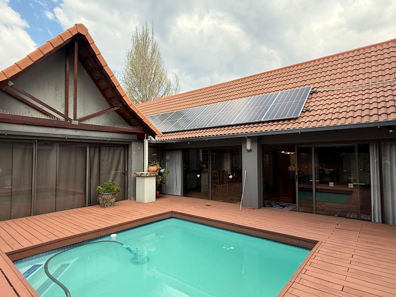 A well-maintained outdoor pool area featuring timber decking, integrated solar panels on the tiled roof, and large sliding glass doors leading to the interior.