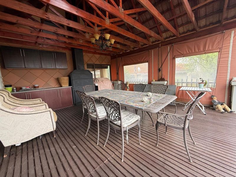 Covered outdoor patio featuring timber decking, exposed roof trusses, built-in braai, and integrated cabinetry, ideal for alfresco dining and entertaining.