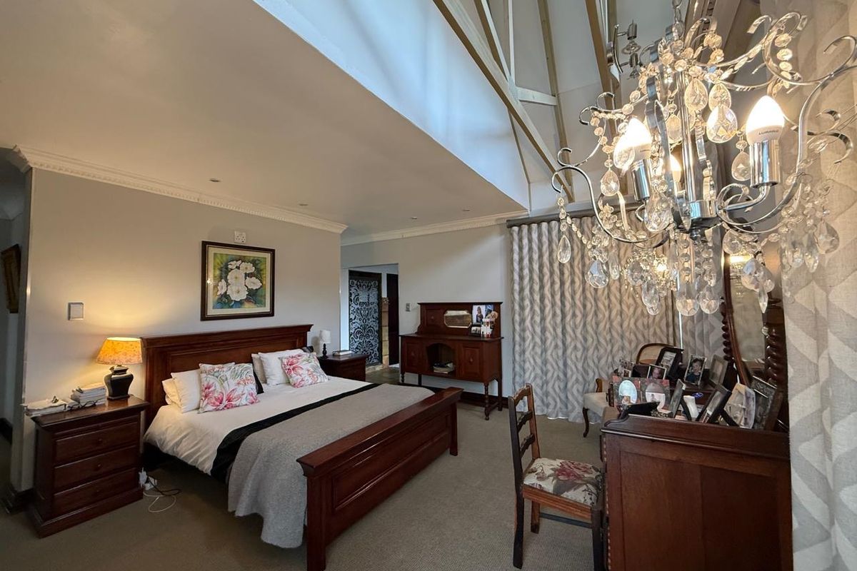 Spacious bedroom featuring a high vaulted ceiling with exposed timber rafters, elegant cornicing, and a prominent crystal chandelier.