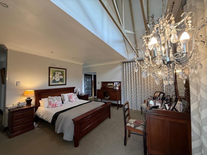 Spacious bedroom featuring a high vaulted ceiling with exposed timber rafters, elegant cornicing, and a prominent crystal chandelier.