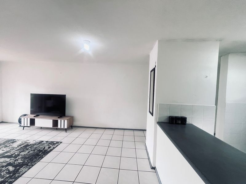 Open plan living area featuring tiled flooring and a kitchen breakfast bar with tiled splashback.