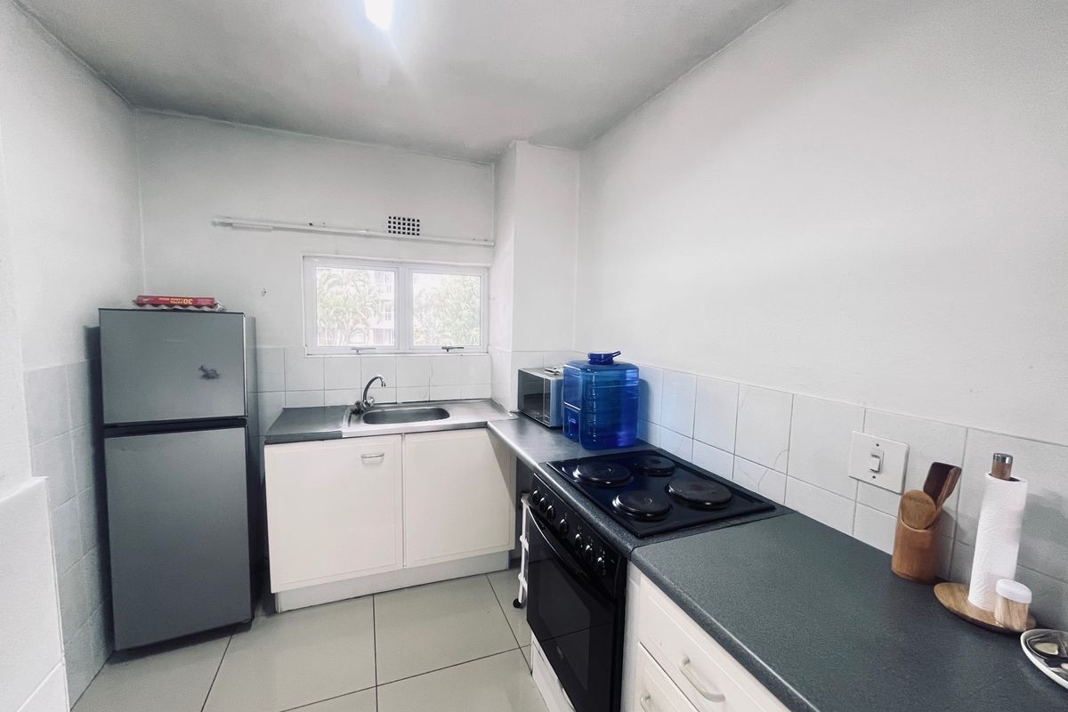 A functional kitchen featuring built-in cabinetry, a stainless steel sink, and an integrated electric stove and oven with tiled splashbacks.