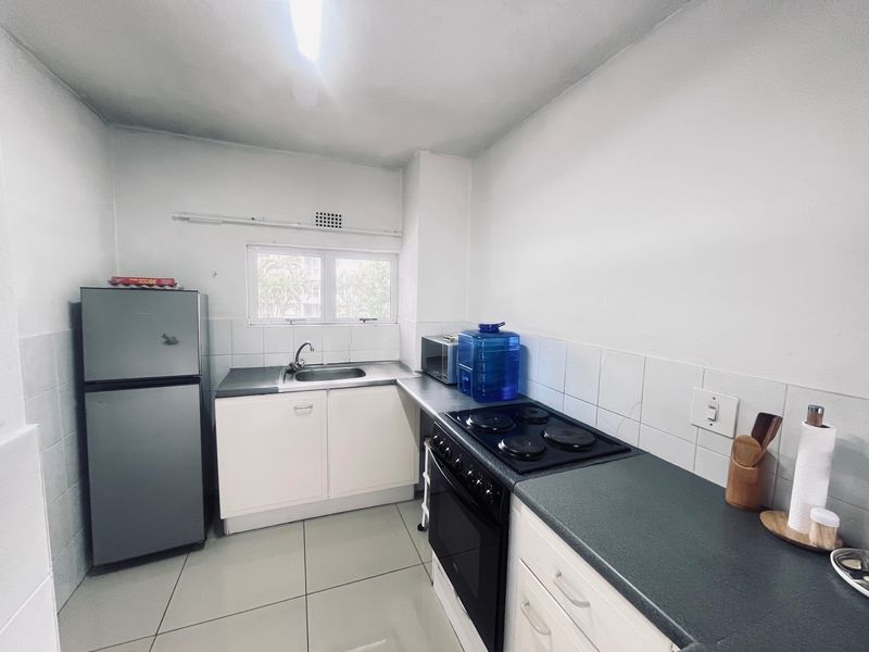 A functional kitchen featuring built-in cabinetry, a stainless steel sink, and an integrated electric stove and oven with tiled splashbacks.