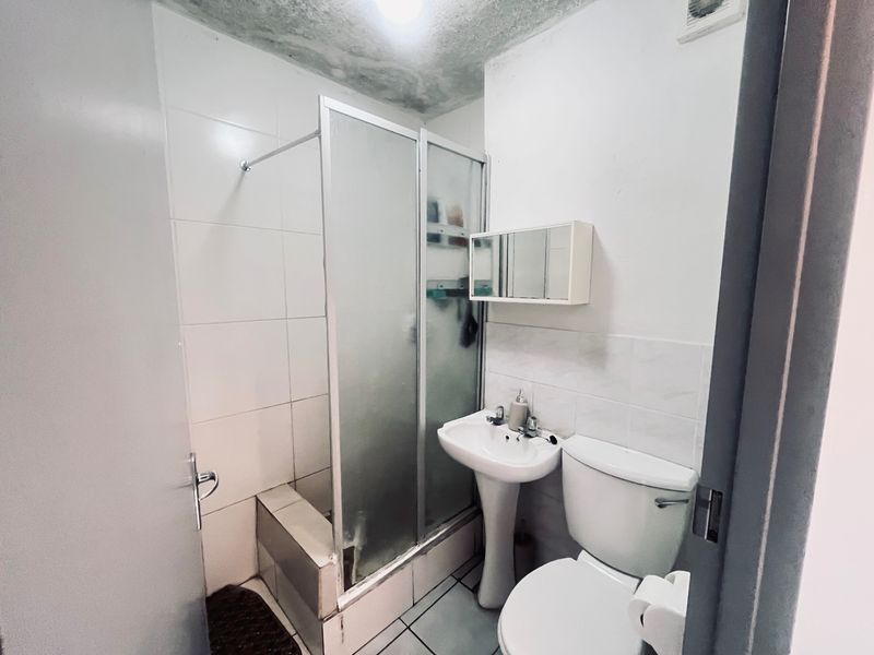 Compact bathroom featuring a pedestal sink, toilet, and shower enclosure. The ceiling shows signs of water damage and requires maintenance.