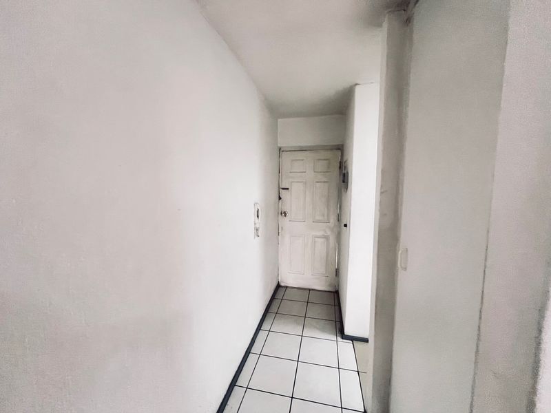 A simple, empty apartment hallway featuring tiled flooring and a white panelled entrance door.